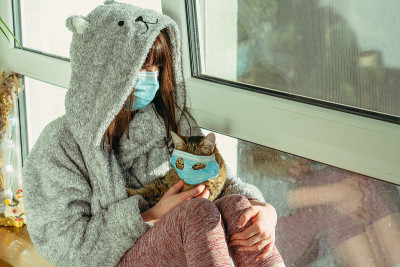 隔离。一位戴着医用防护面具的妇女和一只猫坐在窗台上。