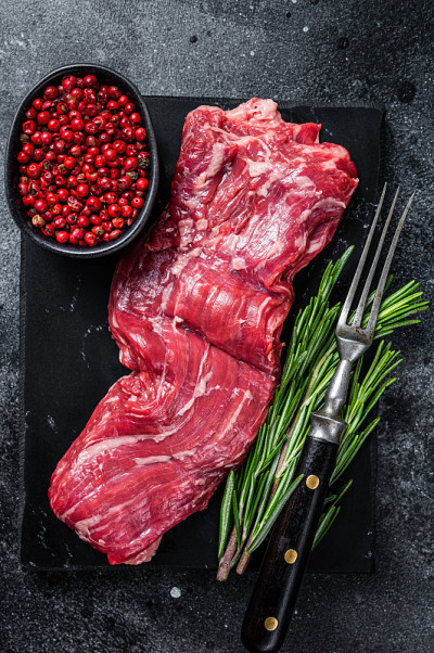 生弯刀裙牛肉牛排大理石板。黑色背景。俯视图