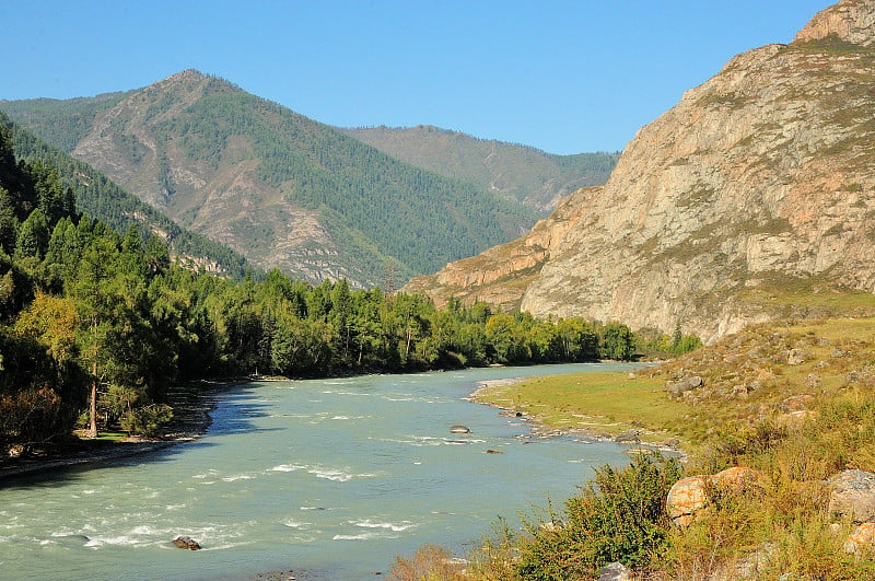 一条美丽的山间河流蜿蜒的河床，静静地流过风景如画的群山环抱的山谷。