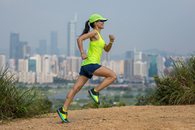 女超级马拉松运动员在现代城市旁边的山上跑步