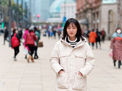 在上海南京路步行街，一个年轻的中国女孩把手放在口袋里看着相机。