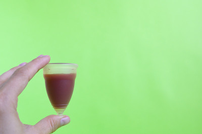 绿色背景上的女人手拿经血杯。空间的文本