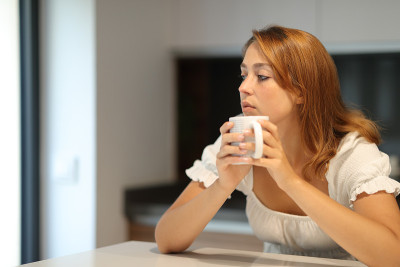 沉思严肃的女人在家里拿着杯子