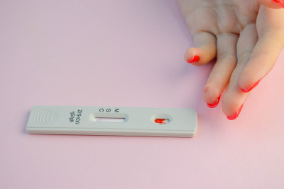 冠状病毒检测位于粉红色背景上。试纸上有一滴血。对冠状病毒的快速诊断。家用测试诊断感染。旁边那个涂着红