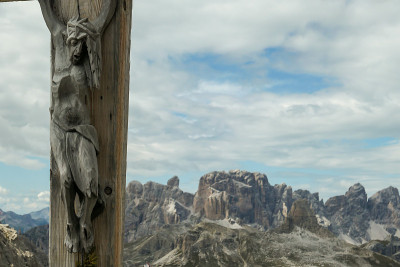 一个木制十字架，上面有耶稣的形象，意大利Dolomites的全景。周围有陡峭的山坡。天空中布满了柔和