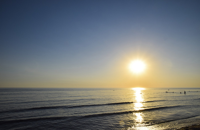 海上日落。傍晚日落时，人们在海里洗澡。