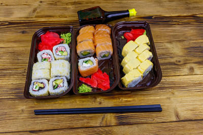 塑料盒子里的寿司卷，酱油和筷子放在木桌上。装在塑料容器内的寿司供外卖或运送