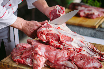 在餐馆里，一个厨师用刀切肉