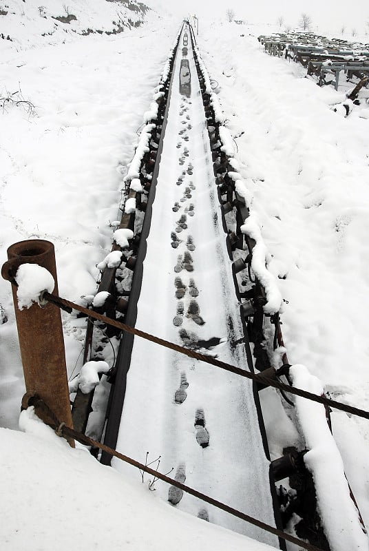 一枚被雪覆盖的地雷。煤矿冬季景观。雪地上有人的脚印。白雪覆盖的传送带。