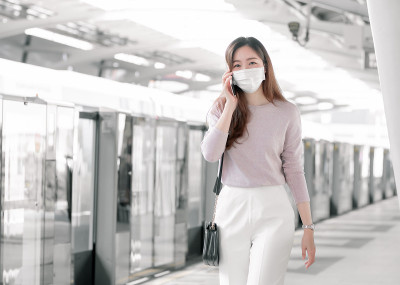 一名女子戴着口罩，站在火车站上打电话