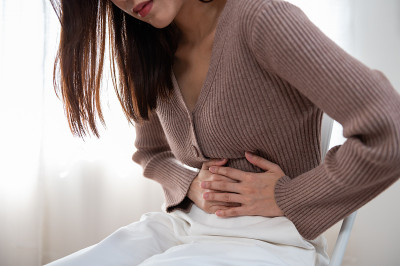 保健医疗或日常生活理念:坐在沙发上收胃痛或月经痛的年轻女士。
