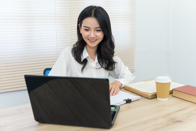 年轻开朗的亚洲学生女大学生在大学图书馆的自习室学习做她的作业和准备考试。