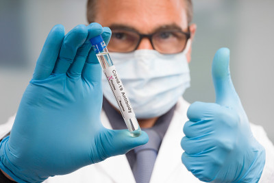 戴医用口罩和医用手套的科学家或医生在实验室前处理带有抗体结果标记的病毒试管，背景中竖起大拇指