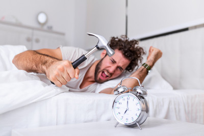 Young man tries to break the alarm clock with hamm