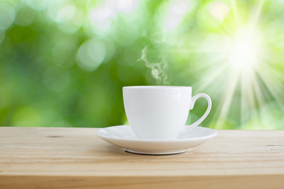 桌上一杯热咖啡，绿色散焦，背景是阳光。