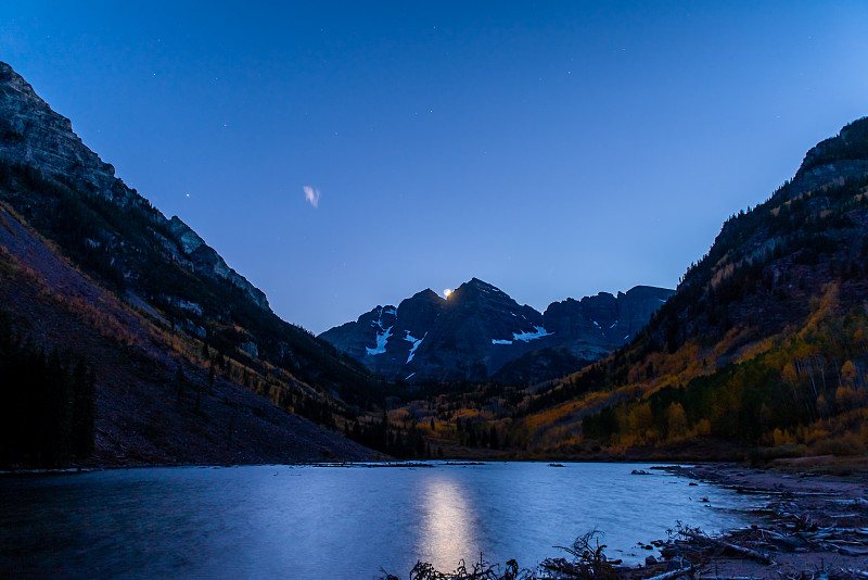 2019年10月，在科罗拉多州阿斯彭的栗色铃铛湖的山峰上，夜幕中有岩石山脉和秋叶，天空中有月亮的路径