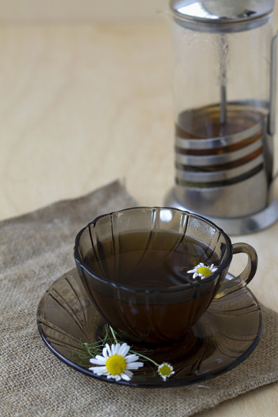 在一张有复印空间的轻木桌上，放上一杯凉茶和甘菊茶。茶杯和茶壶，鲜花和绿叶在黄色的背景。垂直