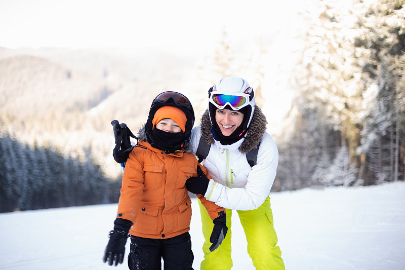 妈妈和儿子穿着滑雪装备在滑雪坡上。