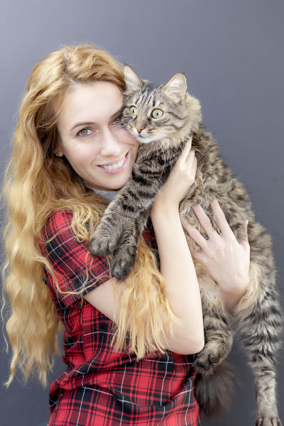 一位快乐的女士抱着一只惊讶的虎斑家猫。爱猫
