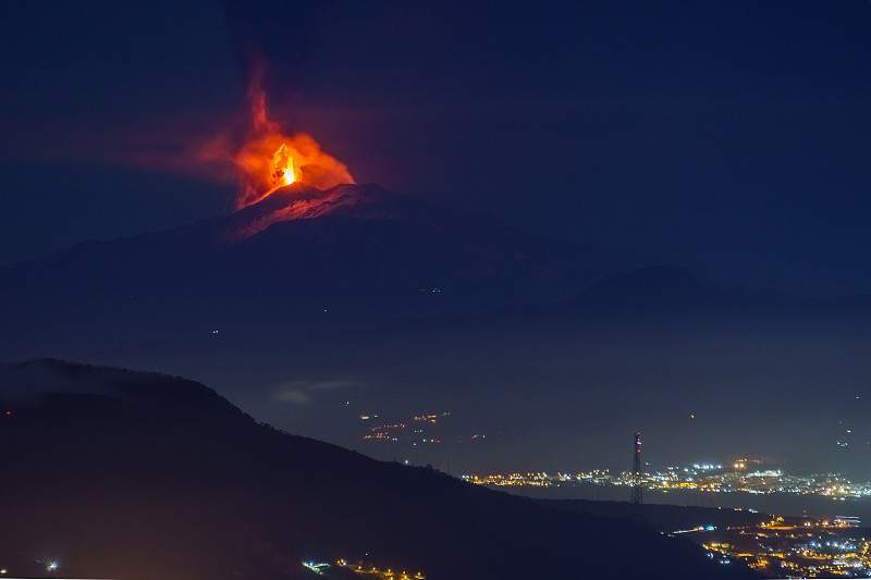 2022年2月10日，意大利西西里岛，埃特纳火山在夜间喷发，前景是大海和城市的灯光