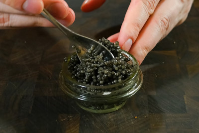 用勺子在玻璃罐中搅拌黑鱼子酱。