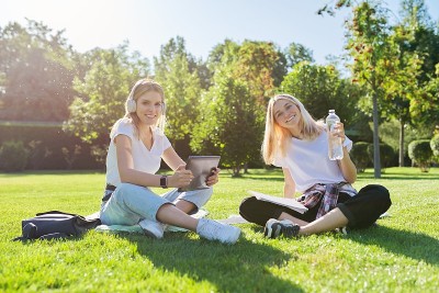 女生们坐在绿色的草坪上拿着数码平板电脑，喝着瓶装水