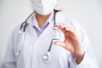 一名戴着口罩的女医生站在实验室里，手里拿着一瓶保护冠状病毒的疫苗。预防COVID-19传播的概念。