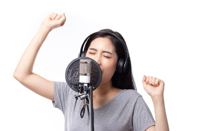 年轻的亚洲女子与麦克风录音歌曲在音乐工作室快乐的表情脸孤立在白色的背景。