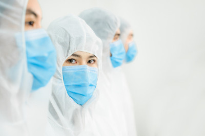 亚洲医学科研人员在实验室穿着安全服，双手交叉站成一排。