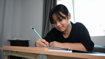 微笑的年轻女孩坐在她的床上做作业。