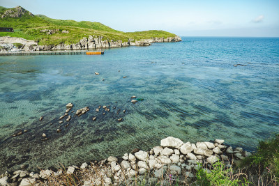 夏天海洋全景。一个浅浅的，清澈的，透明的海洋，周围有礁石，岩石和绿色的山丘。日本海洋。