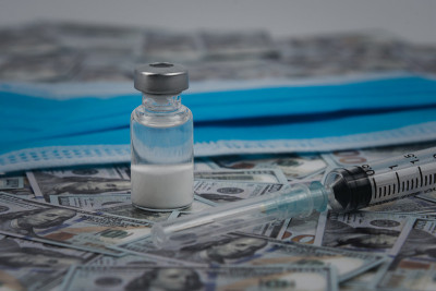 装有covid-19疫苗的瓶子和印在美钞上的注射器供背景使用。用于预防COVID-19的新型冠状病毒