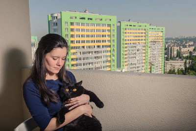 一个带着黑猫的女孩从阳台看向一座新楼