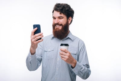 兴奋的男子拿着一杯咖啡用智能手机