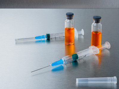 银色铝制背景的橙色冠状病毒疫苗注射器和安瓿。