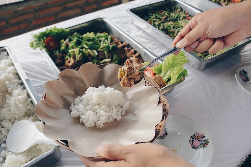 餐厅午餐时，人用手将烤鸡肉串从钢锅中放入木纸盘中