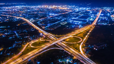 环城高速公路和高速公路的互通和移动的前照灯汽车运输，在夜间城市景观蓝色背景鸟瞰图
