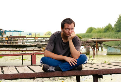 在一个温暖的夏日，一个年轻人坐在河上的桥上。在户外休息。