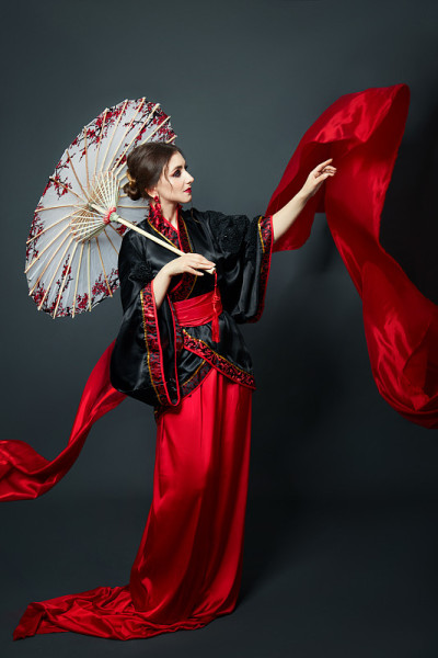 女人穿着红色的中国日本民间服装。飘逸的织物，漂亮的雨伞和扇子，日本中式风格，耳朵上的长耳环。女孩在黑