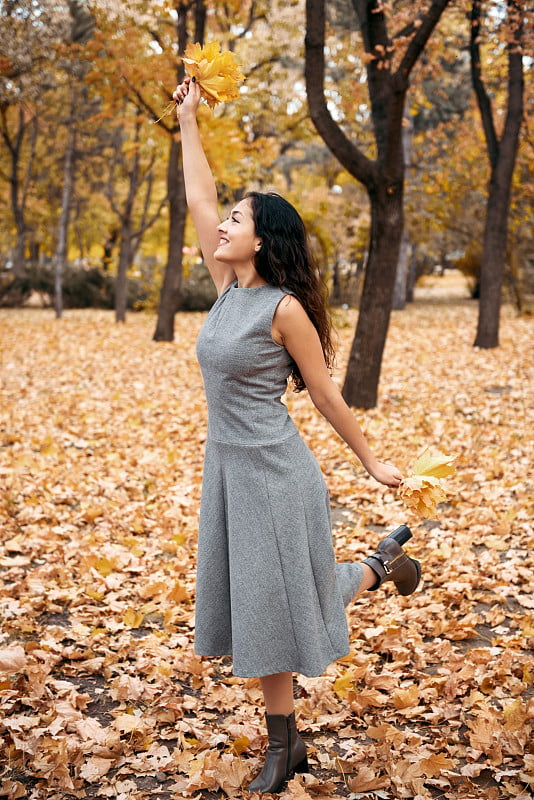 漂亮的女人摆姿势与枫叶在秋天公园附近的大树。美丽的风景在秋天季节。