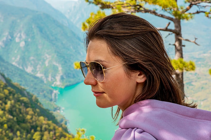 女徒步旅行者戴着太阳镜在山的观点与湖泊和峡谷的背景