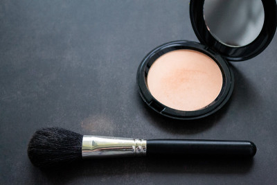 A black makeup brush next to an open box with a mi