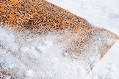 雪中地毯的特写镜头。红色的旧波斯地毯被倒过来，撒上雪来清洁它