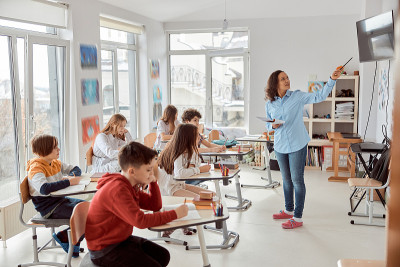 当老师在教室里讲课时，快乐的孩子们坐在桌子旁。小学生坐在课桌上