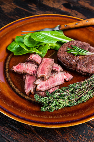 里脊肉、烤里脊肉和切好的牛肉与沙拉放在盘子里。深色木制背景。俯视图