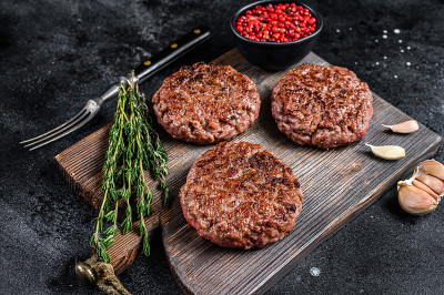烧烤用碎肉和香草做成的汉堡牛肉饼放在木板上。黑色背景。俯视图