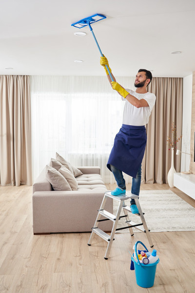一名男子正在打扫客厅的天花板和灯具。房屋清洁服务理念
