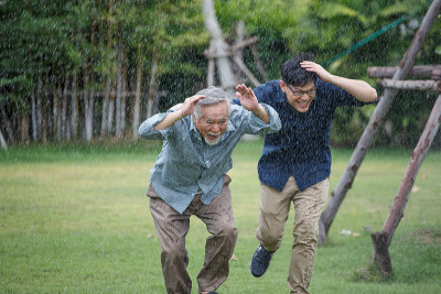 亚洲老人和年轻人在公园里从雨中奔跑。快乐亚年幼的儿子和年老的父亲一起在雨中避雨