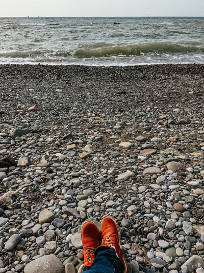 穿着红靴子的脚在海边。从岩石海滩看海景。旅行的概念。穿着登山鞋的男人或女人都在户外放松。