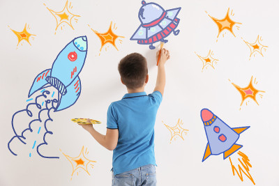 可爱的孩子在室内白墙上画宇宙飞船